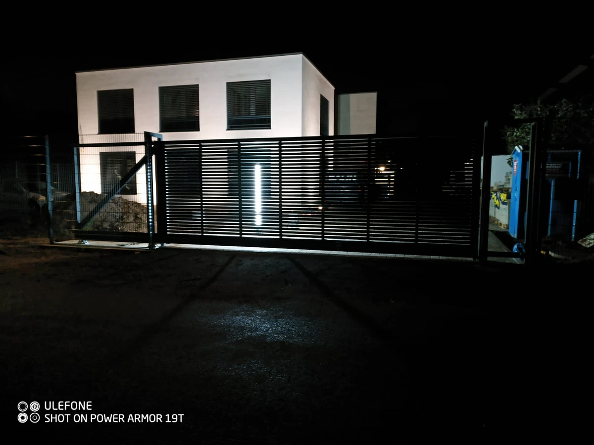 Modernes Schiebetor mit horizontalen Lamellen und LED-Beleuchtung vor modernem Wohnhaus