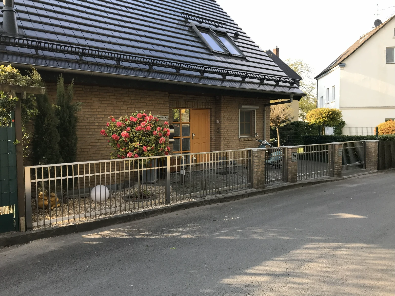 Vorgarten mit elegantem Edelstahl-Zaun als Zäune zwischen Ziegelpfeilern und Rhododendronblüten vor Einfamilienhaus