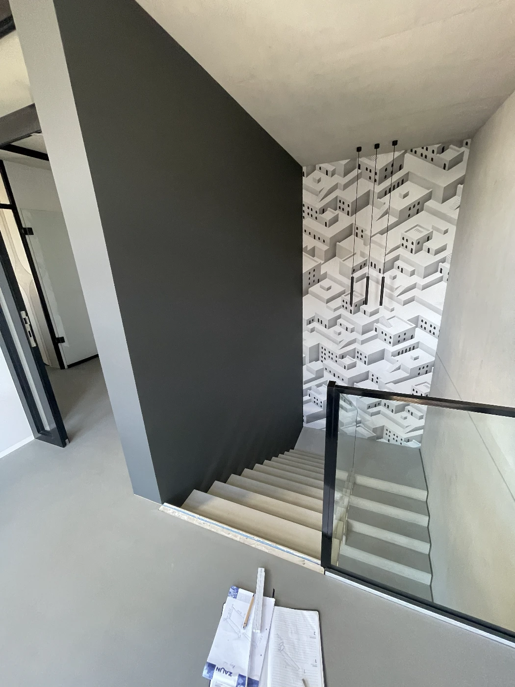 Moderne Innentreppe mit Betonstufen und Glasgeländer vor dunkler Wand und geometrischer Fototapete