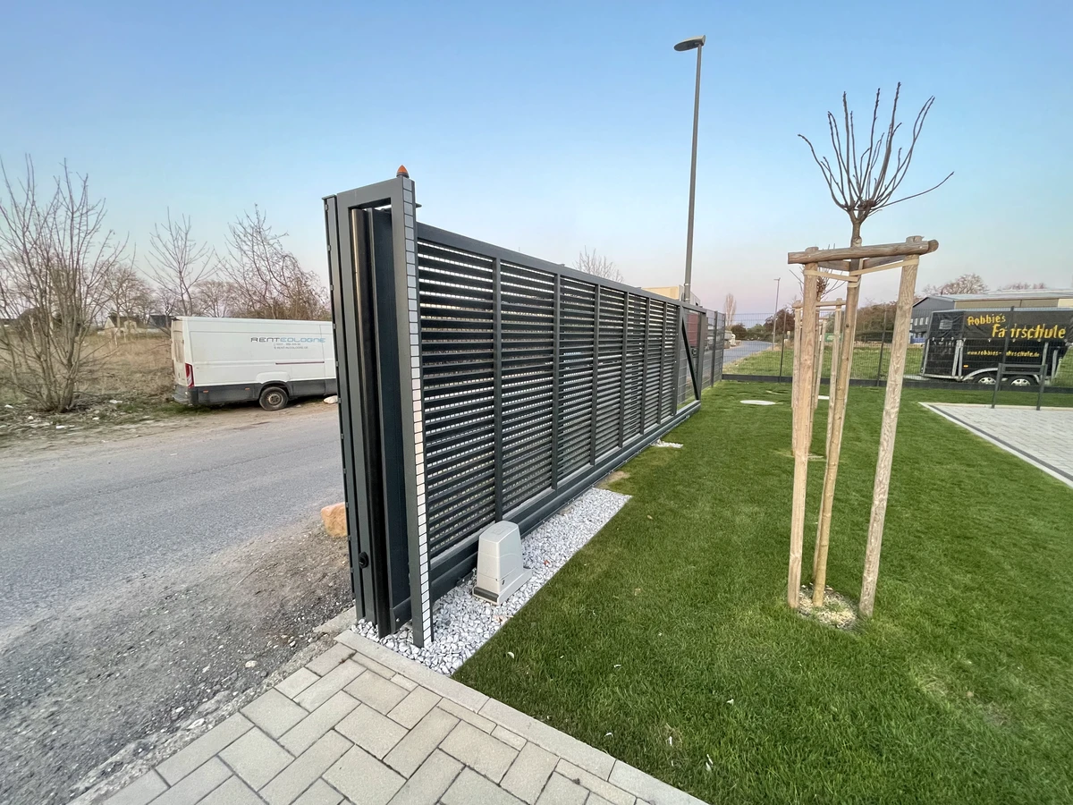 Automatisches Schiebetor aus Metall als Grundstückszufahrt neben Rasenfläche und gepflastertem Weg