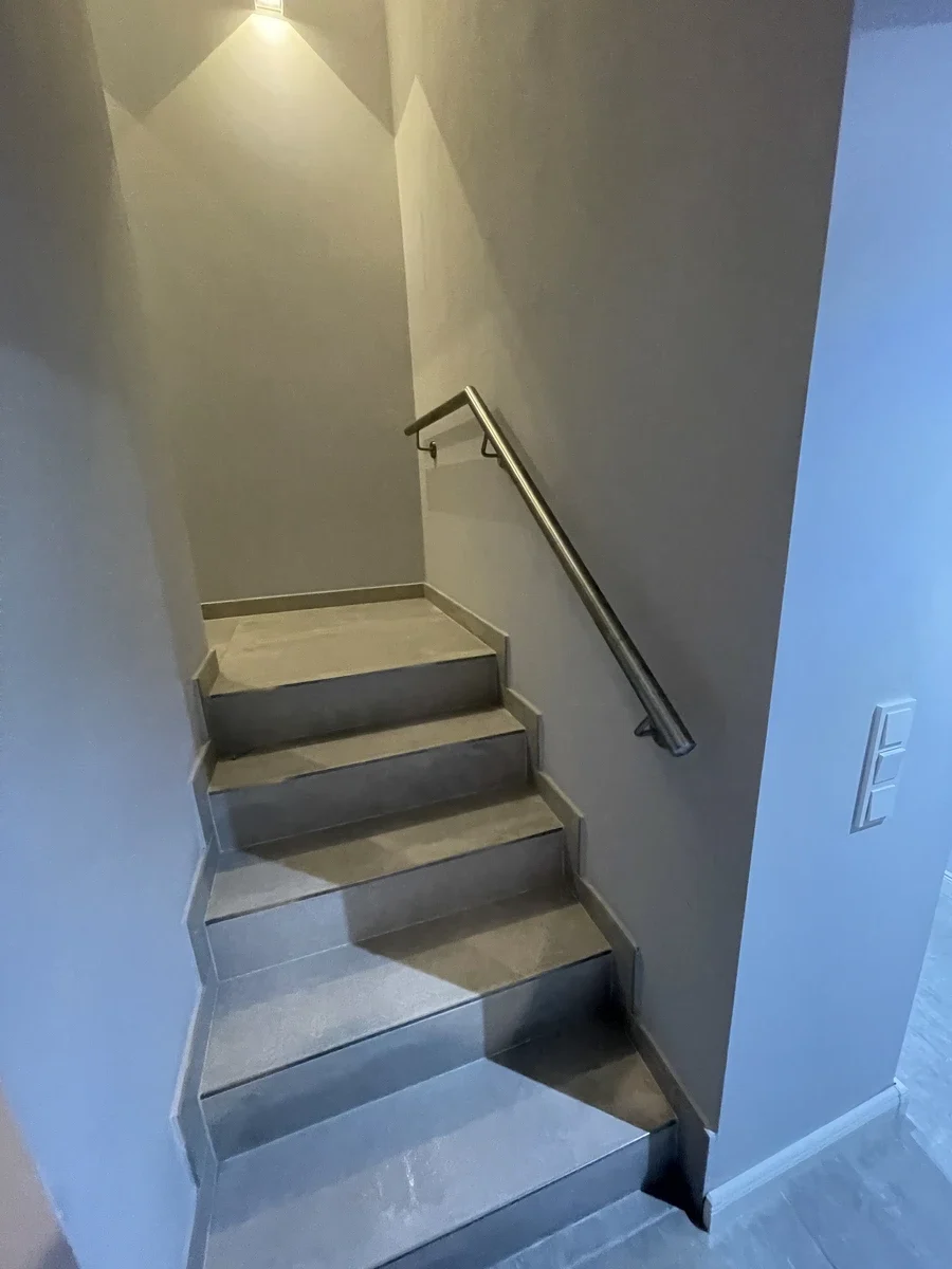 Moderne Innentreppe mit grauen Fliesenstufen und schlankem Edelstahlgeländer