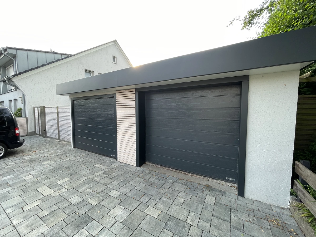 Moderne Doppelgarage mit anthrazitfarbenen Sektionaltoren und gepflasterter Auffahrt