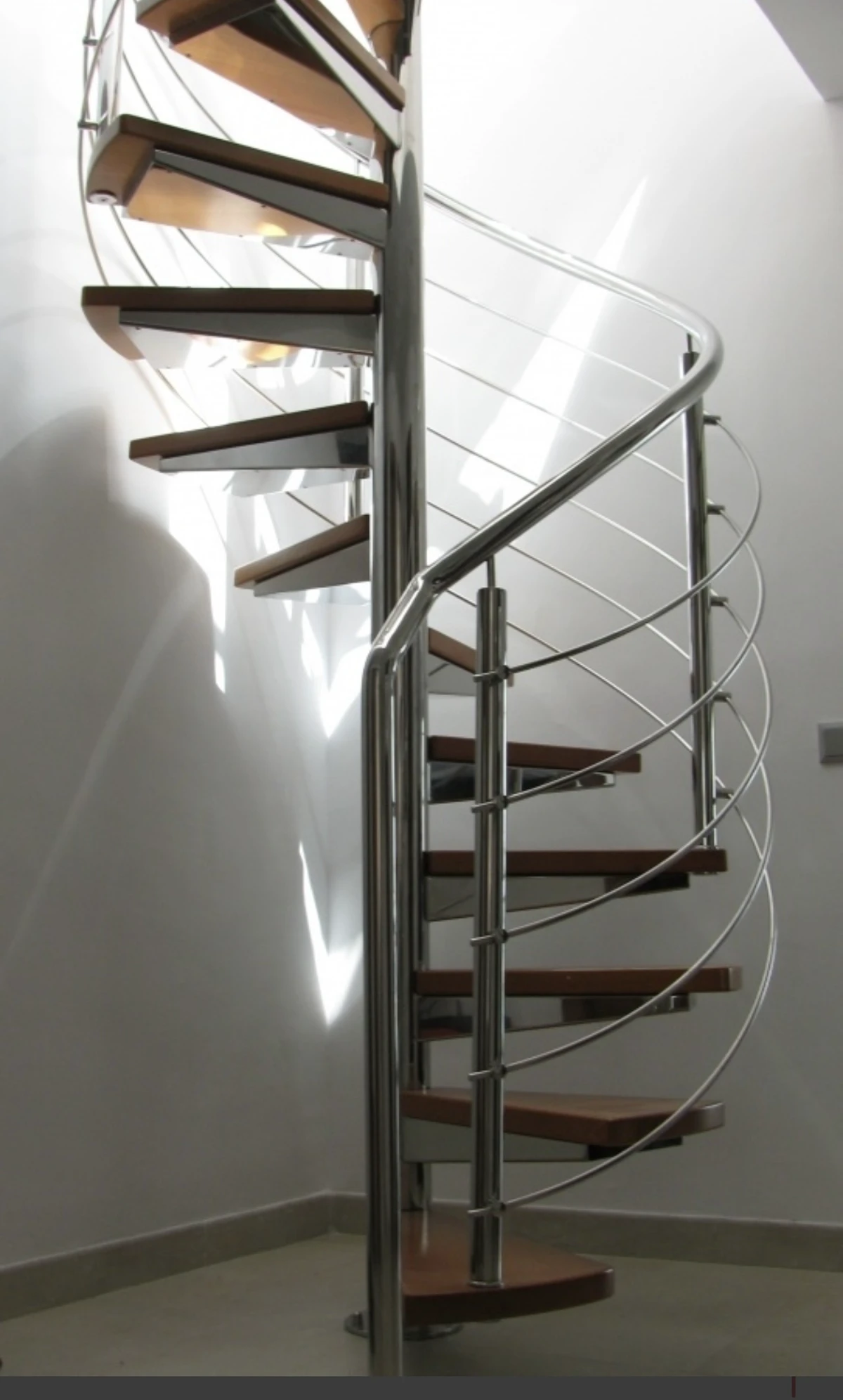 Moderne Spindeltreppe mit Holzstufen und filigranem Edelstahlgeländer in heller Raumecke