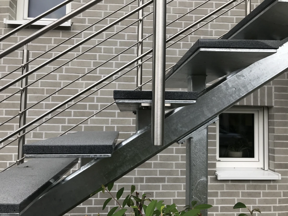 Außentreppe mit freitragenden Stufen und Edelstahlgeländer vor hellgrauer Klinkerwand
