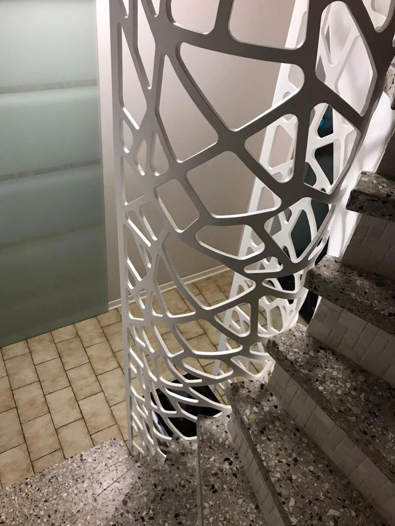 Filigrane Innentreppe mit grauen Terrazzo-Stufen und organisch perforiertem weißen Metallgeländer