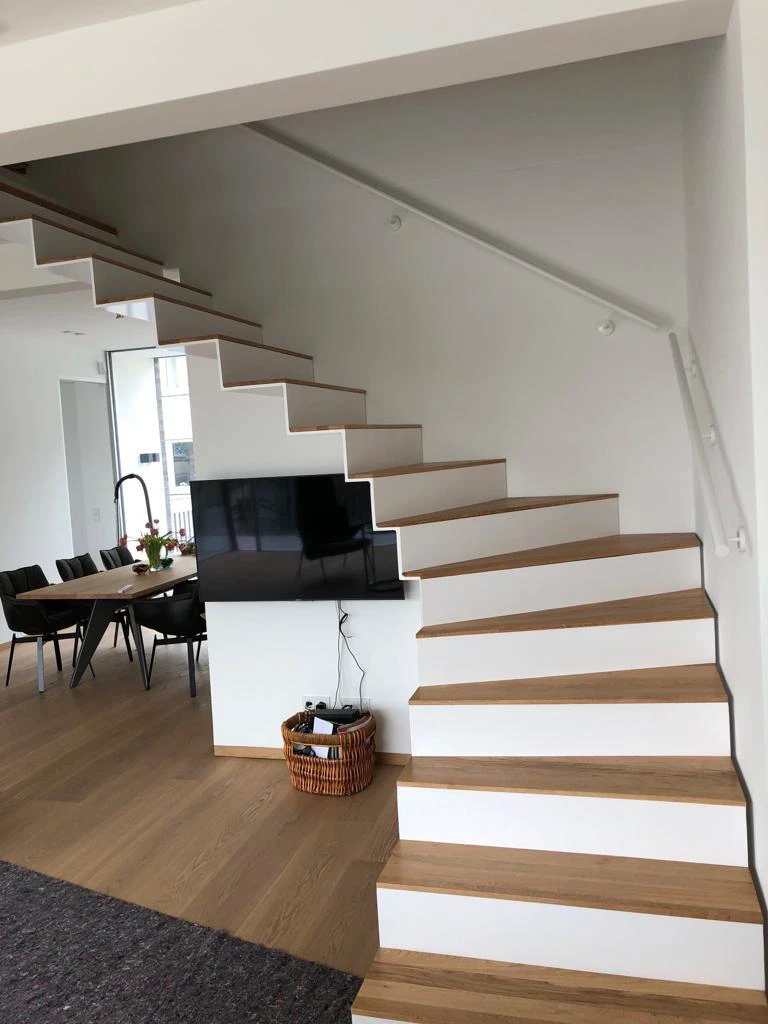 Minimalistische Kragarmtreppe mit Holzstufen und weißem Metallgeländer in modernem Wohnraum