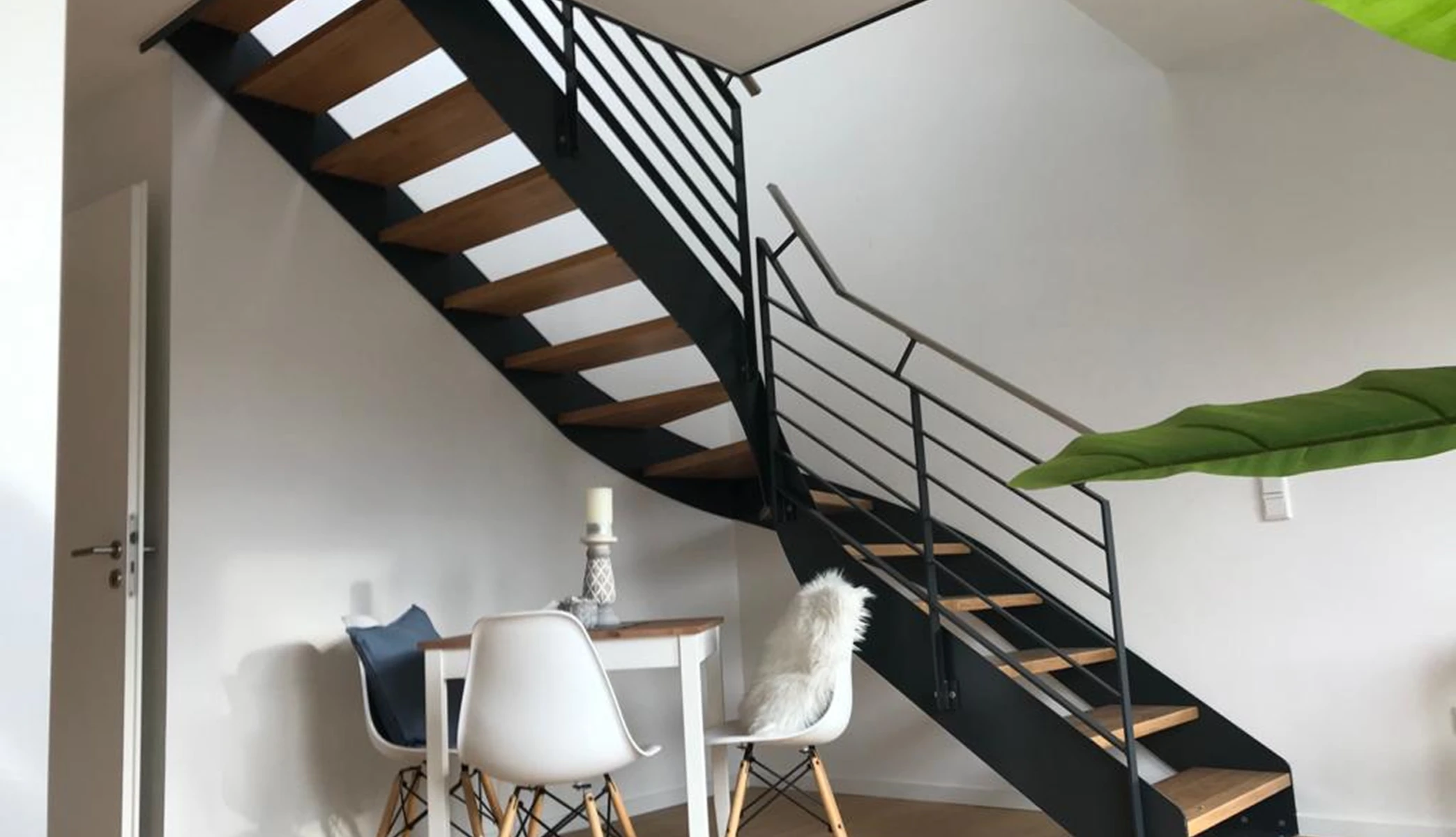 Offene Innentreppe mit schwarzen Stahlwangen, Holzstufen und Edelstahlgeländer neben Esstisch