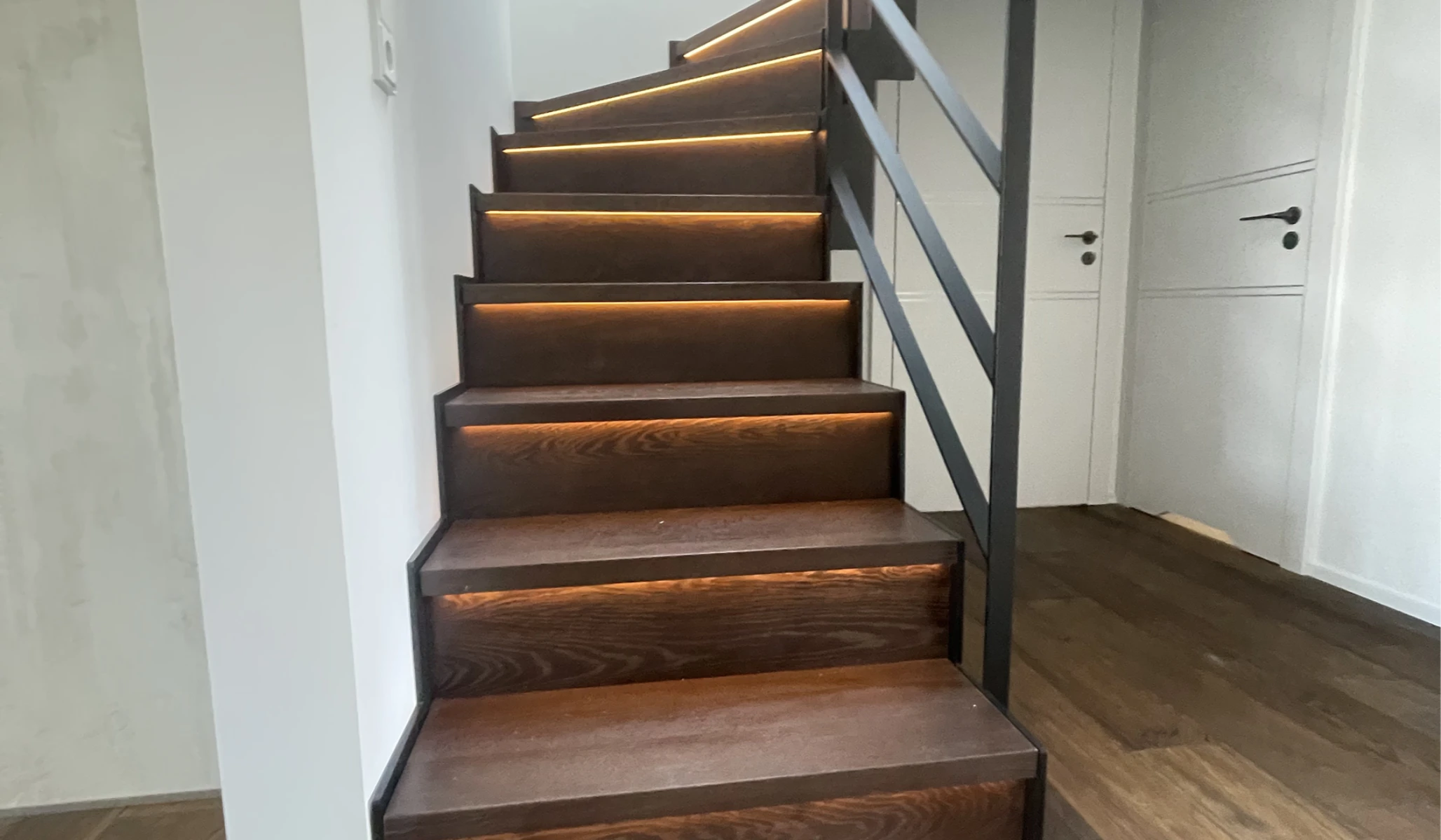 Moderne Wangentreppe aus dunklem Holz mit integrierter LED-Beleuchtung und Metallgeländer